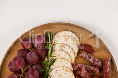 Crispy biscuits, cherry tomatoes, grapes and bowl of cheese on wooden board