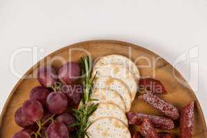 Crispy biscuits, cherry tomatoes, grapes and bowl of cheese on wooden board