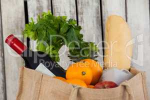 Wine bottle, fruits and vegetables with bread loaf in grocery bag