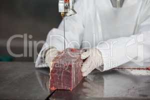 Female butcher cutting raw meat on a band saw machine