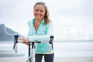 Portrait of happy woman standing with bicycle on beach