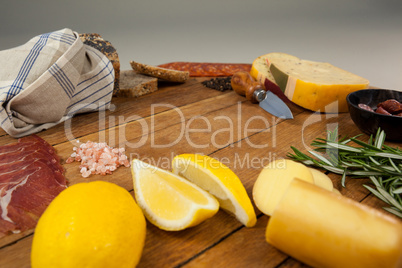 Cheese, ham, lemon, and bread with various ingredients on chopping board