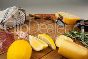 Cheese, ham, lemon, and bread with various ingredients on chopping board
