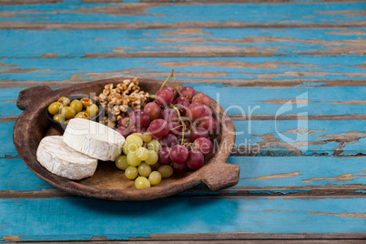 Cheese, grapes, olives and walnuts in wooden bowl