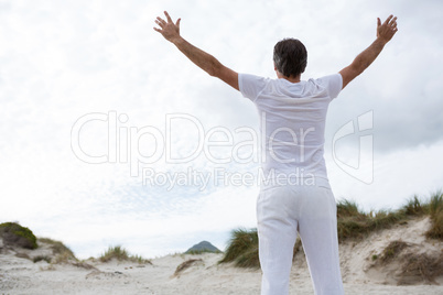 Rear view of man standing with arms outstretched on beach