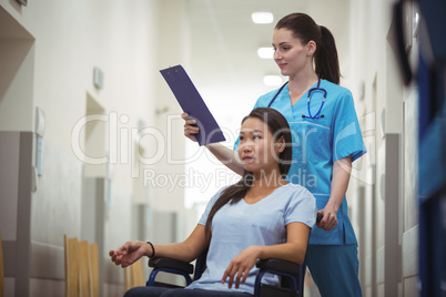 Female nurse assisting patient on wheelchair in corridor