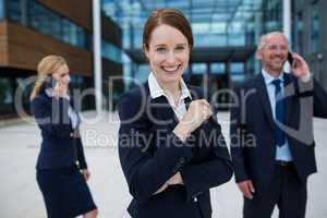 Businesswoman smiling at camera while colleagues talking on mobile phones