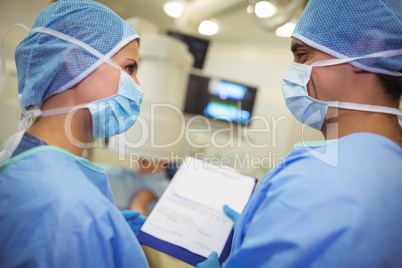 Male and female surgeons having discussion over clipboard