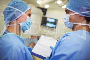 Male and female surgeons having discussion over clipboard