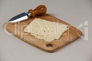 Slices of cheese with knife on chopping board