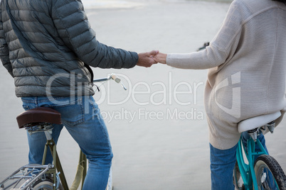 Mid section of couple holding hands on bicycle at beach