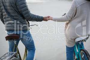 Mid section of couple holding hands on bicycle at beach