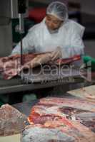 Female butcher cutting raw meat on a band saw machine