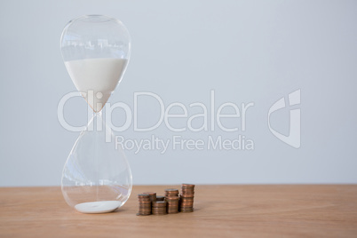 Hourglass and stacks of coins on table