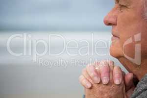 Thoughtful senior man with hands clasped at the beach
