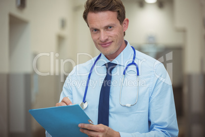 Portrait of male doctor writing on clipboard in corridor