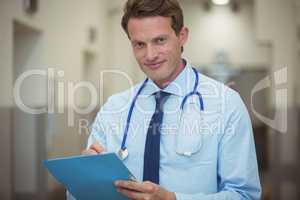 Portrait of male doctor writing on clipboard in corridor