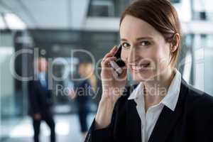Smiling businesswoman talking on mobile phone in office corridor