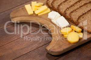 Slices of brown bread and variety of cheese on wooden chopping board