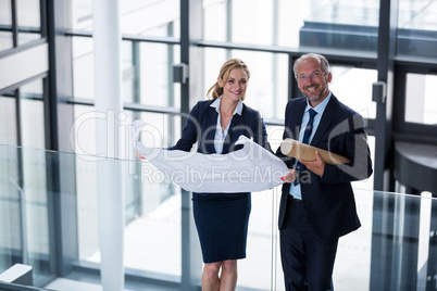 Portrait of business colleagues standing with blueprint in corridor