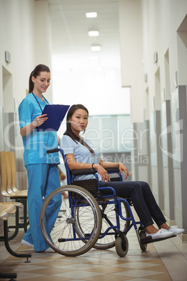 Female nurse assisting patient on wheelchair in corridor