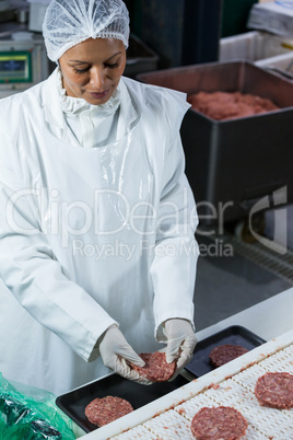 Female butcher arranging hamburger patty on tray