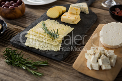 Variety of cheese, olives, biscuits and rosemary herbs on wooden table