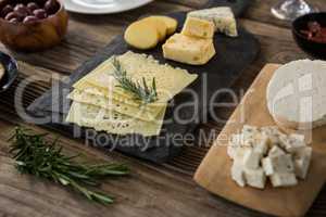 Variety of cheese, olives, biscuits and rosemary herbs on wooden table