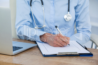 Mid section of doctor writing on clipboard