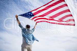 Rear view of man holding american flag on beach