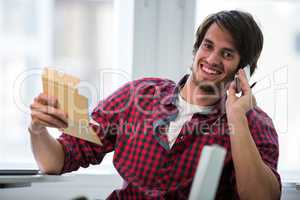 Graphic designer talking on mobile phone and writing in a diary at his desk