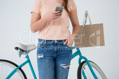 Woman with shopping bag and bicycle using mobile phone