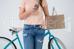 Woman with shopping bag and bicycle using mobile phone