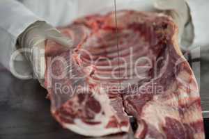 Female butcher cutting raw meat on a band saw machine