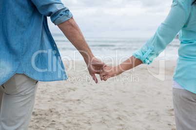 Mid section of couple holding hands on beach