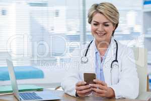 Female doctor using mobile phone with laptop on table