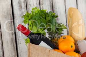 Wine bottle, fruits and vegetables with bread loaf in grocery bag