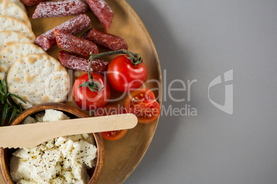 Crispy biscuits, cherry tomatoes, grapes and bowl of cheese on wooden board