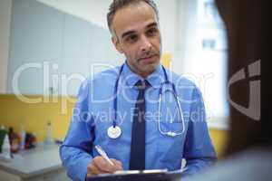 Doctor interacting with patient and writing on clipboard