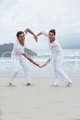 Romantic couple making heart by hands on beach