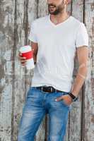 Man in white t-shirt and blue jeans holding a disposable coffee cup