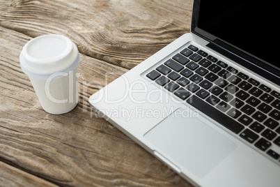 Disposable coffee cup and laptop on wooden table