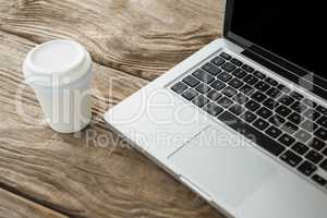 Disposable coffee cup and laptop on wooden table