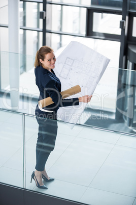 Businesswoman standing at office corridor with blueprint