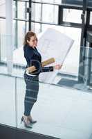 Businesswoman standing at office corridor with blueprint