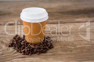 Coffee beans with disposable coffee cup on wooden table