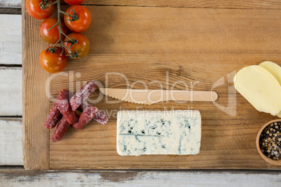 Roquefort cheese, wooden knife, cherry tomatoes and meat on chopping board