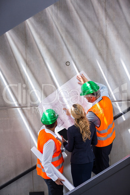 Businesswoman and architects standing on a staircase discussing with blueprint