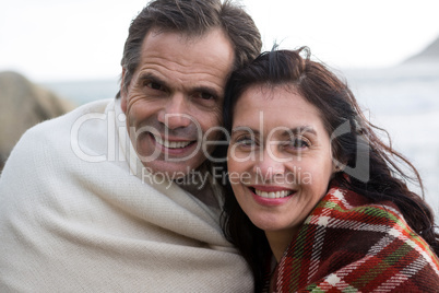 Portrait of happy couple wrapped in shawl on beach