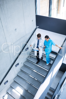 Doctor and nurse discussing over a report while climbing down stairs